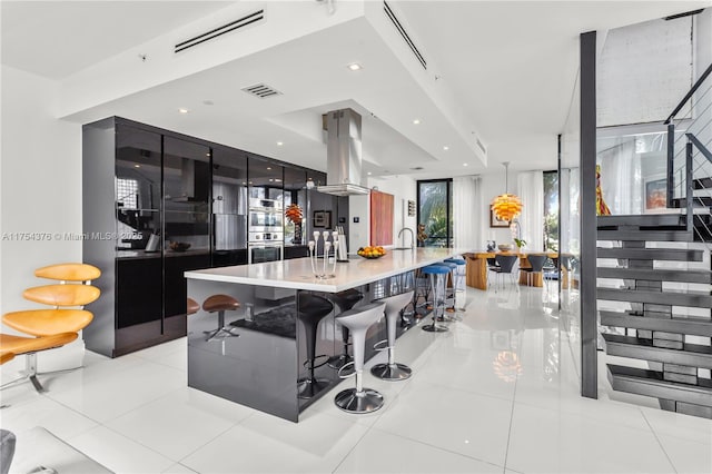 kitchen featuring stainless steel double oven, island range hood, visible vents, light countertops, and modern cabinets