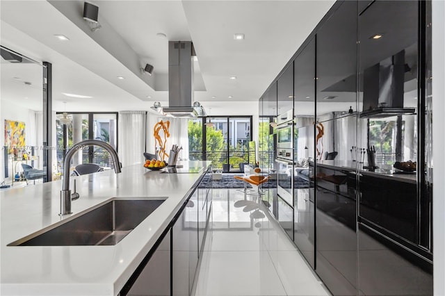 kitchen featuring light tile patterned floors, island exhaust hood, black electric cooktop, dark cabinetry, and a sink