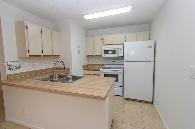 kitchen featuring light tile patterned floors, cream cabinets, a sink, white appliances, and a peninsula