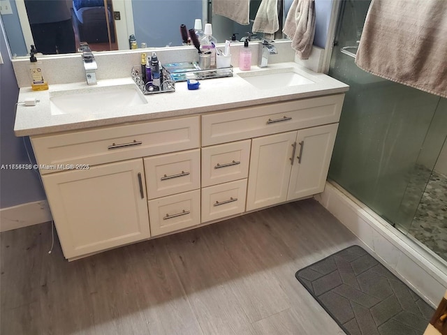 full bath with double vanity, wood finished floors, a shower stall, and a sink