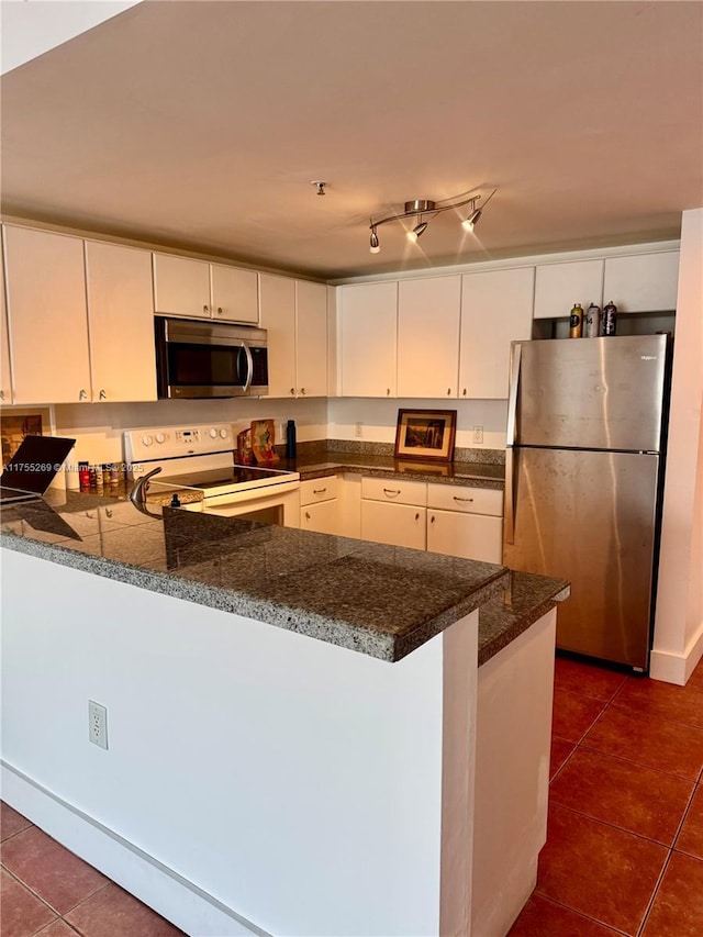 kitchen with dark stone counters, white cabinets, a peninsula, stainless steel appliances, and dark tile patterned floors