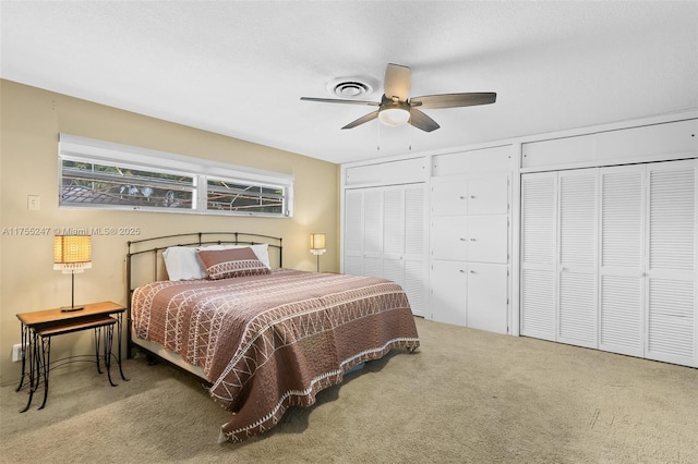 bedroom featuring ceiling fan, visible vents, two closets, and carpet flooring