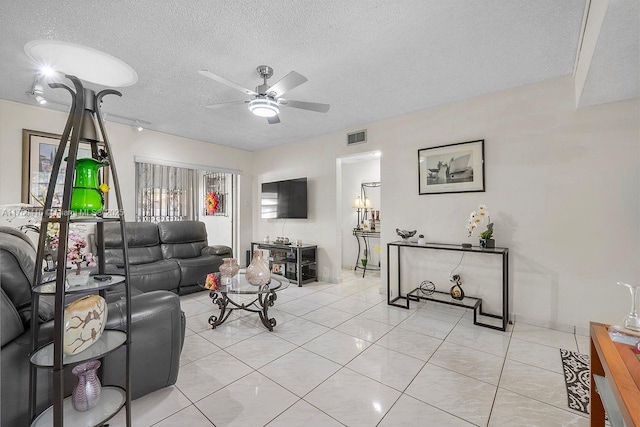 living area featuring light tile patterned floors, ceiling fan, visible vents, and a textured ceiling