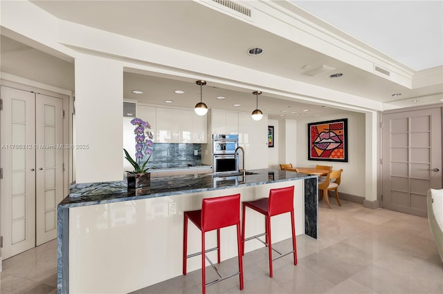 kitchen featuring visible vents, backsplash, double oven, dark stone countertops, and a kitchen bar