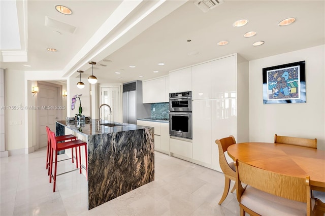 kitchen with a kitchen bar, a sink, visible vents, and white cabinetry