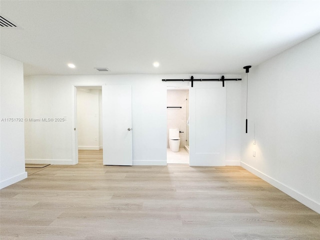 spare room featuring a barn door, baseboards, and wood finished floors