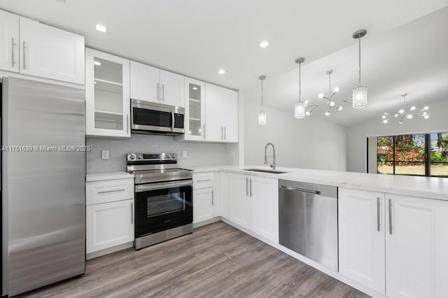 kitchen with stainless steel appliances, wood finished floors, a sink, light countertops, and decorative light fixtures