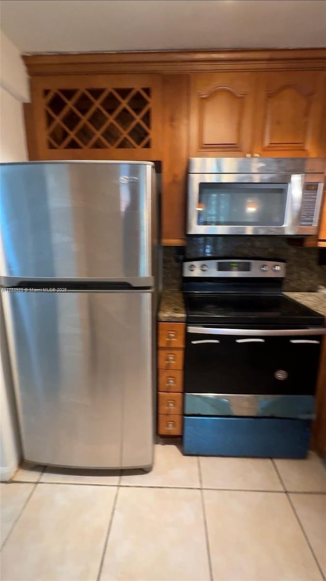 kitchen featuring backsplash, light tile patterned flooring, brown cabinetry, and appliances with stainless steel finishes