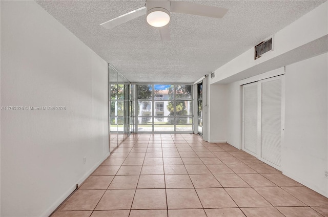 empty room with visible vents, ceiling fan, expansive windows, light tile patterned flooring, and a textured ceiling