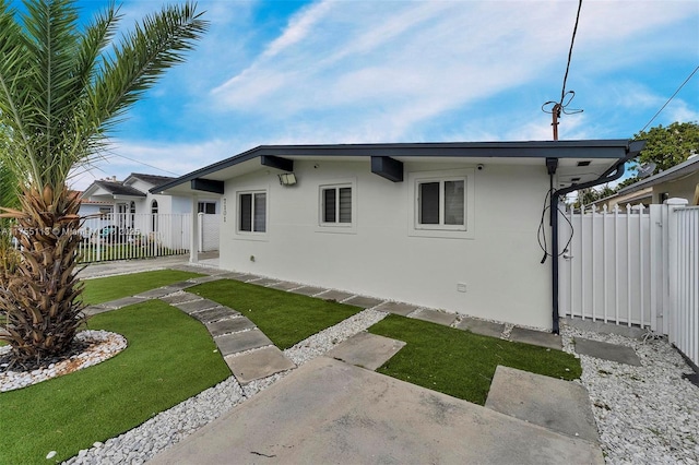 rear view of property with a lawn, fence, and stucco siding