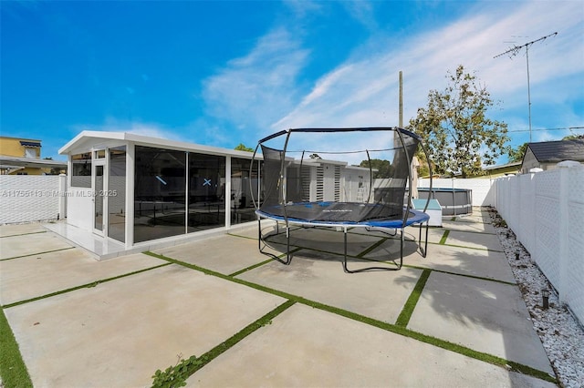 view of patio / terrace with a sunroom, a fenced backyard, and a trampoline