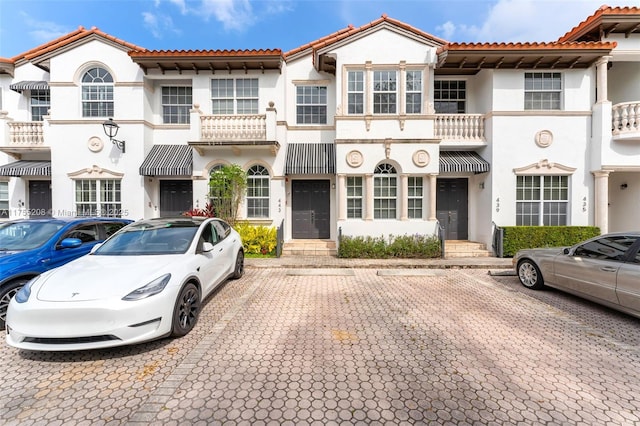 view of front facade featuring a balcony, a tile roof, uncovered parking, and stucco siding