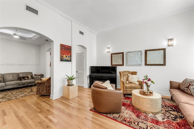 living room with arched walkways, wood finished floors, visible vents, baseboards, and crown molding