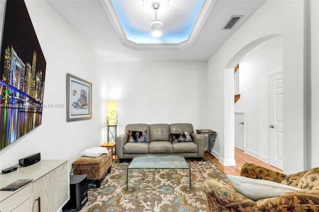 living area with arched walkways, a tray ceiling, visible vents, wood finished floors, and baseboards