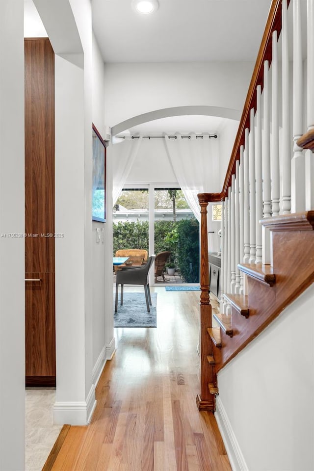 entrance foyer with baseboards, arched walkways, stairs, and light wood-style floors