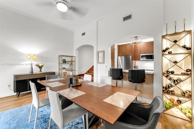 dining room featuring visible vents, arched walkways, ceiling fan, stairway, and light wood-style floors