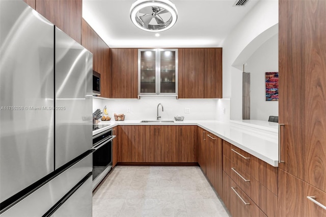 kitchen with modern cabinets, glass insert cabinets, stainless steel appliances, light countertops, and a sink