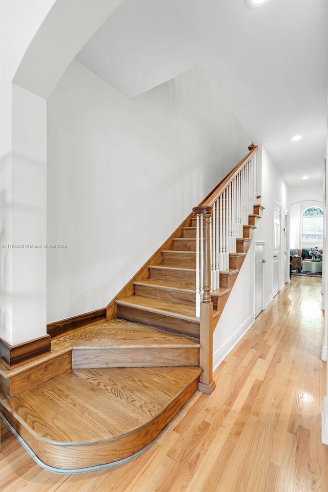 staircase featuring baseboards, arched walkways, and wood finished floors