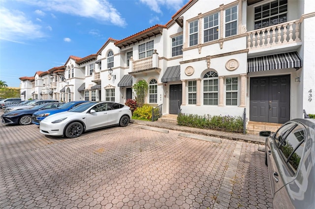 view of front facade with a tiled roof, uncovered parking, and stucco siding