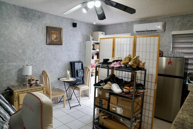 interior space with light tile patterned floors, an AC wall unit, ceiling fan, and freestanding refrigerator