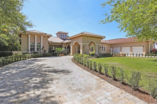 mediterranean / spanish house featuring a garage, a front yard, decorative driveway, and stucco siding