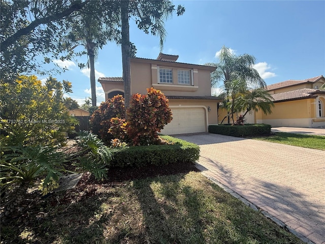 mediterranean / spanish-style home with a tiled roof, decorative driveway, an attached garage, and stucco siding