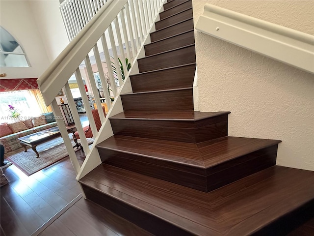 stairway with a high ceiling, wood finished floors, and a textured wall