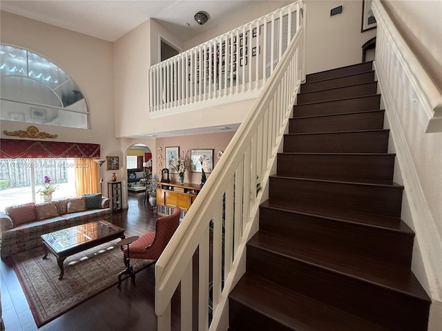 staircase featuring arched walkways, a towering ceiling, and wood finished floors