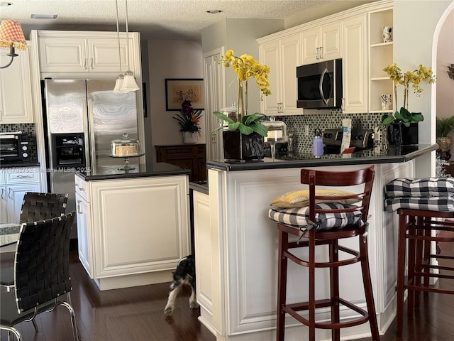 kitchen with dark wood-style flooring, decorative backsplash, a center island, stainless steel microwave, and dark countertops