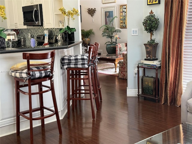 kitchen with decorative backsplash, dark countertops, dark wood-style floors, stainless steel microwave, and a kitchen breakfast bar