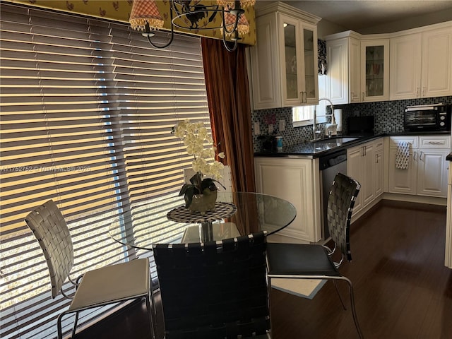 kitchen featuring dark countertops, dark wood-style floors, glass insert cabinets, a sink, and backsplash