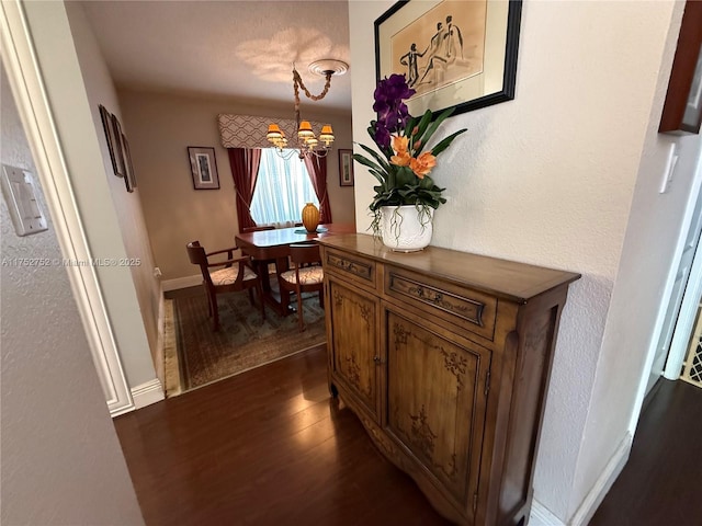 corridor with a chandelier, dark wood finished floors, and baseboards