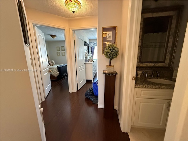 corridor featuring a textured ceiling, baseboards, dark wood-style flooring, and a sink