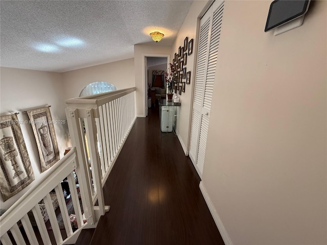 corridor with a textured ceiling, baseboards, and wood finished floors