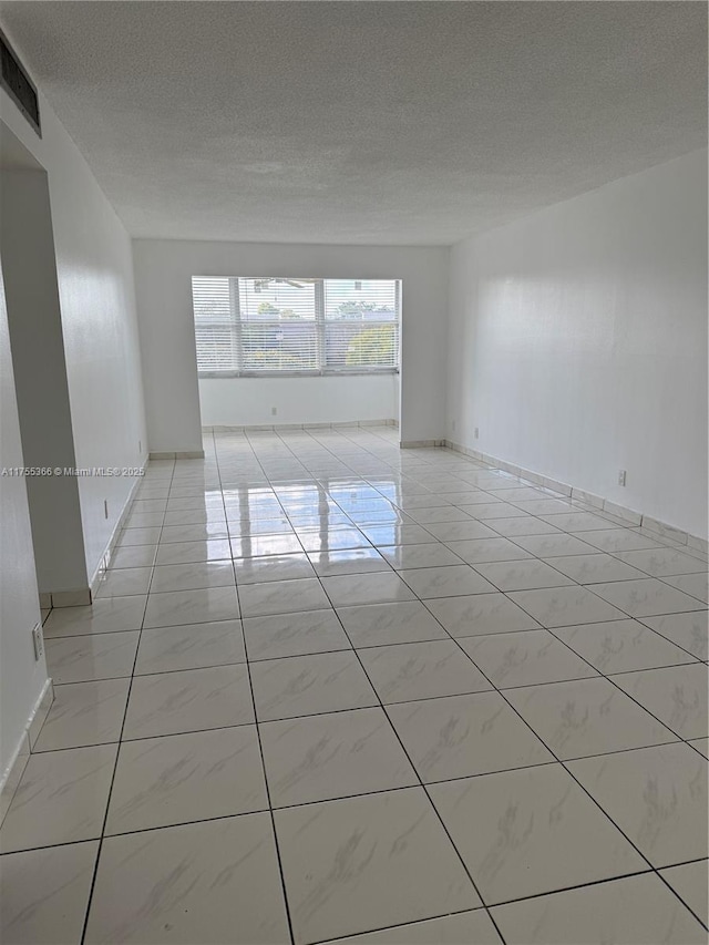 unfurnished room with a textured ceiling, light tile patterned floors, and baseboards