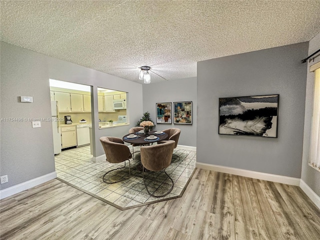 dining area with light wood-style flooring, baseboards, and a textured ceiling