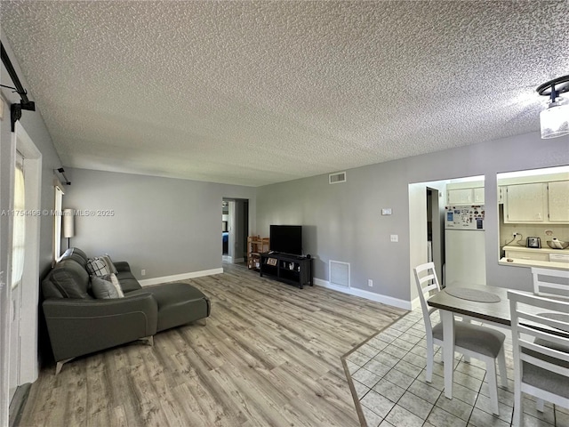 living room with a textured ceiling, light wood-style flooring, visible vents, and baseboards