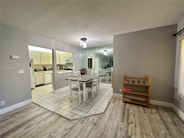 dining area featuring light wood-type flooring, a textured ceiling, and baseboards