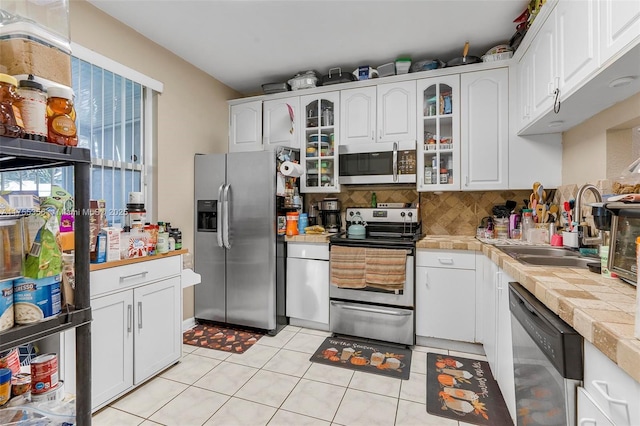 kitchen featuring a sink, white cabinets, appliances with stainless steel finishes, backsplash, and glass insert cabinets