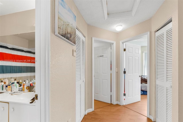 hall featuring a textured ceiling, light wood finished floors, a sink, and baseboards