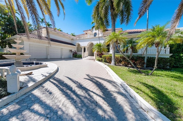 mediterranean / spanish-style house featuring stucco siding, a tile roof, decorative driveway, a front yard, and an attached garage