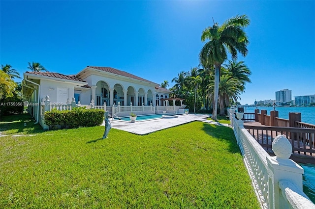 rear view of property featuring stucco siding, a water view, a tile roof, a yard, and an outdoor pool