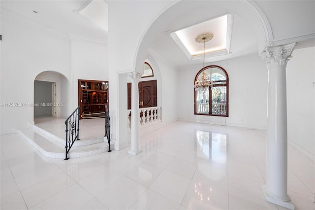 foyer entrance with tile patterned flooring, a raised ceiling, and decorative columns