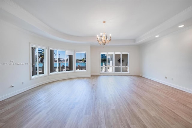 unfurnished room with light wood-type flooring, a tray ceiling, baseboards, and an inviting chandelier