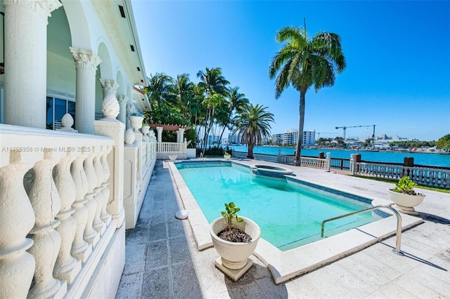 view of swimming pool with a patio area, a pool with connected hot tub, fence, and a water view