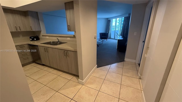 kitchen with light tile patterned floors, baseboards, dishwasher, light countertops, and a sink