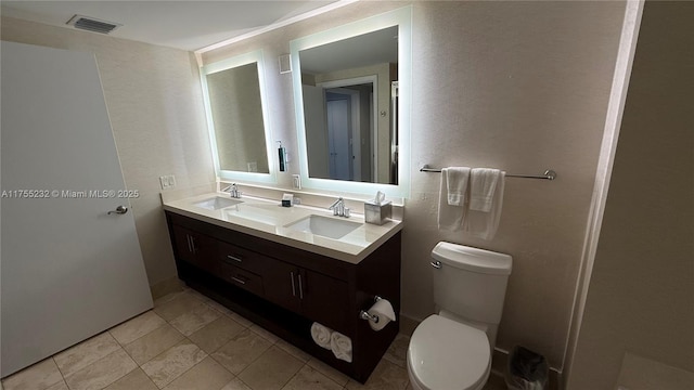 bathroom featuring toilet, double vanity, a sink, and visible vents