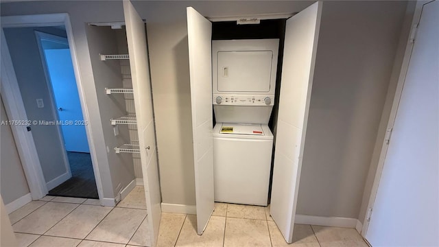 clothes washing area featuring light tile patterned floors, laundry area, baseboards, and stacked washer / drying machine