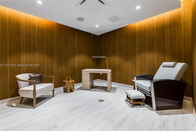 sitting room featuring light wood-type flooring, wood walls, and elevator