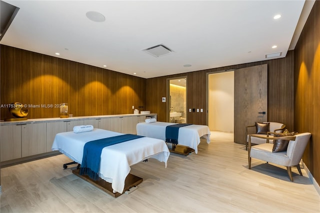 bedroom with light wood-style floors, wooden walls, and visible vents